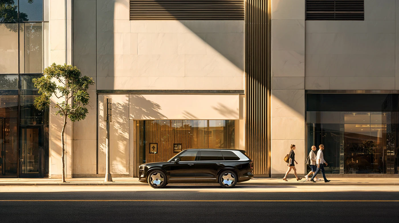 A black Zeekr 9X parked in afternoon sun in front of a pale stone building with a bronze fin, three people walking past.